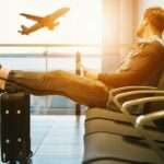 man sitting on gang chair with feet on luggage looking at airplane